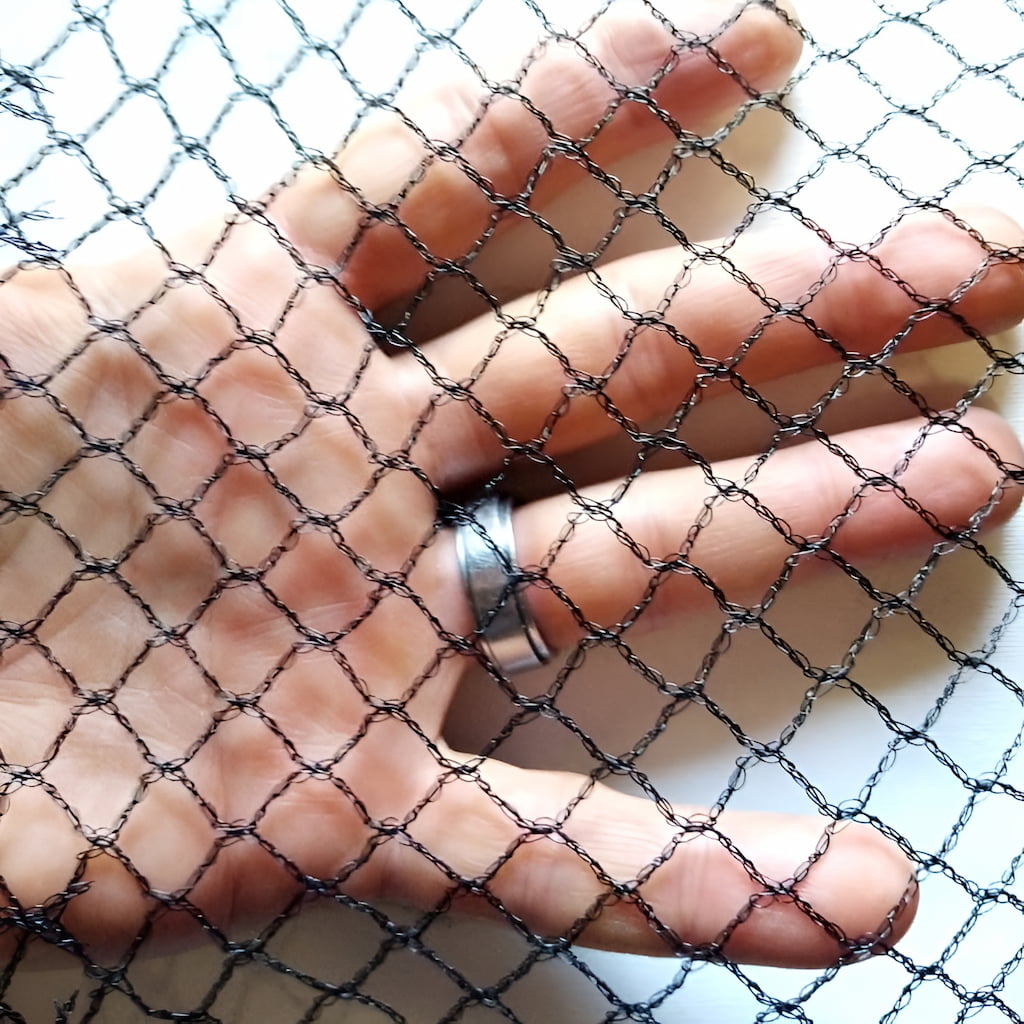 Close up of bird proof netting with hand showing the 1cm square hole size when tensioned.